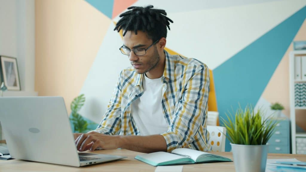 College student focused on work at a laptop in a bright home workspace